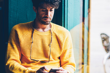 Bearded handsome young man w/ith eyeglasses dressed in yellow sweater reading incoming notification...