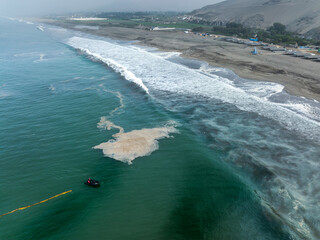 Boat deploying containment barriers against an oil spill at Chancay beach, Lima, Peru. Efforts to...