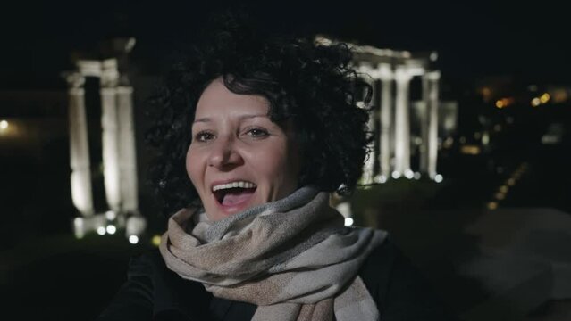 Selfie of happy smiling woman at night tour of Roman forum with background view of Tample of Saturn in Rome, Italy, slow motion