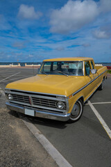 pick-up vintage,  américain des années 60, de couleur jaune sur un parking en bord de mer