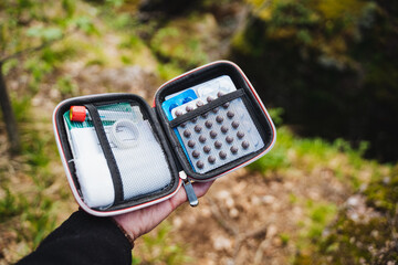 Hand holding a portable first aid kit with various medical supplies for outdoor adventures. Be prepared with medication, bandages, antiseptic, and more for safety in nature