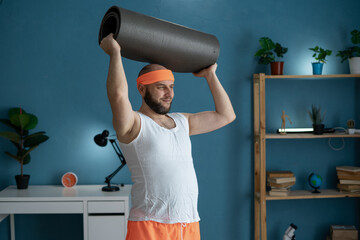 Man working out with yoga mat at home in stylish workout attire, blue background