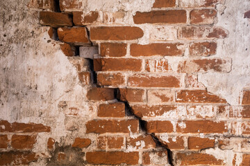 an old brick wall made of red medieval brick with a crack in the middle and peeling plaster