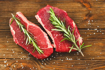 A piece of premium meat, striploin steak on a wooden table with a sprig of rosemary