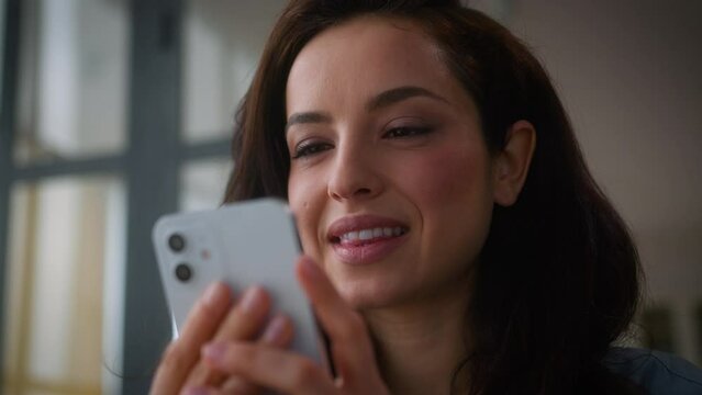 Caucasian happy smiling cheerful girl user influencer female woman smiling laughing bite lip holding mobile phone smile laugh using smartphone cellphone social media fun app online addict at home