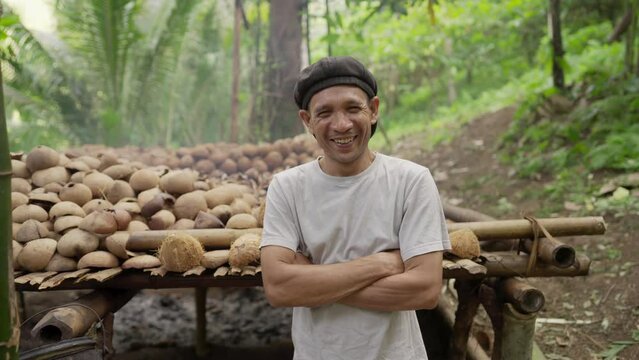 Dolly in, rural portrait of smiling indonesian smallholder farmer with traditional coconut drying rack filled with copra, sustainable agriculture, southeast asia