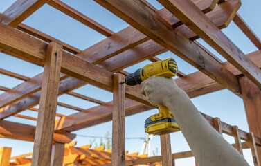 A woman assembles a wooden garden structure using a cordless drill, demonstrating home improvement...