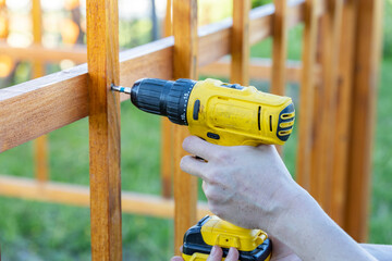 A person is using a drill to attach a wooden fence in a backyard setting. The drill bit is visible...