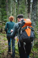Young couple enjoying a hiking adventure in lush green forest with backpacks and hiking poles. Exploring nature, trekking through woodland, and escaping into the serene wilderness