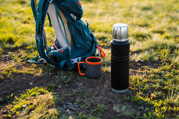 A water bottle lies on the ground next to a thermos and a mug in the natural environment. Nearby,...