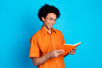 Photo of funky cool guy dressed orange shirt spectacles reading book emtpy space isolated blue...
