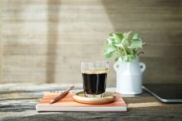 Coffee glass cup and Devil's ivy Golden Pothos and notebook on wooden table and wood background
