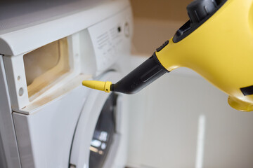 hand in gloves. Using a steam cleaner to clean a washing machine