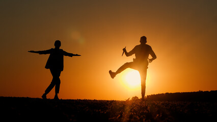 At sunset, the silhouettes of two businessmen can be seen dancing joyfully, one of them clutching a tablet.