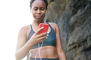 Young woman with dark skin downloading music songs in player on smartphone for morning workout...