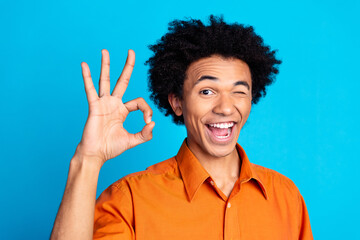 Photo of funky cool guy dressed orange shirt showing okey winking eye emtpy space isolated blue...