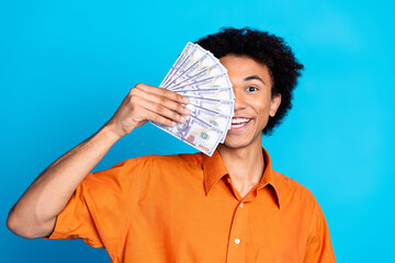 Photo of cheerful positive guy dressed orange shirt rising money fan cover face isolated blue color...