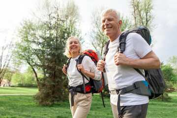 elderly athletic couple of seniors man and woman with hiking backpacks travel in the forest...