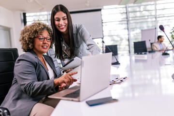 Two multiracial businesswoman working together on laptops and tablets in office