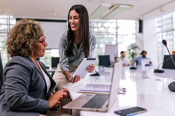 Two multiracial businesswoman working together on laptops and tablets in office