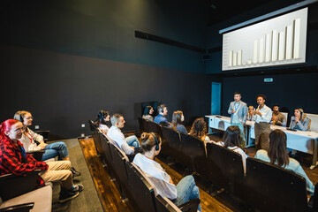 Asian and African American business people having speach on a press conference in a convention center.Diagrams on a smartboard