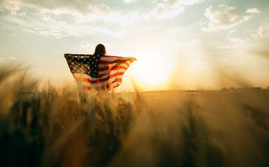 Young happy woman with American flag in a wheat field at sunset celebrate Independence day. 4th of...