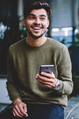 Happy bearded hipster guy excited with good news receiving message on smartphone sitting on urban...