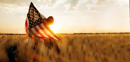 Young woman with American flag in a wheat field at sunset. 4th of July. Patriotic holiday, american...