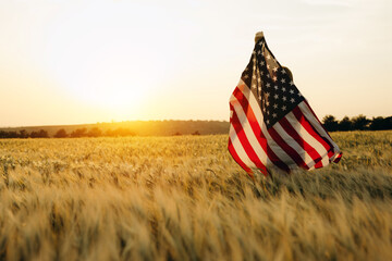 Young happy woman with American flag in a wheat field at sunset celebrate Independence day. 4th of...