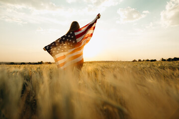 Young happy woman with American flag in a wheat field at sunset celebrate Independence day. 4th of...