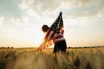 Young happy woman with American flag in a wheat field at sunset celebrate Independence day. 4th of...