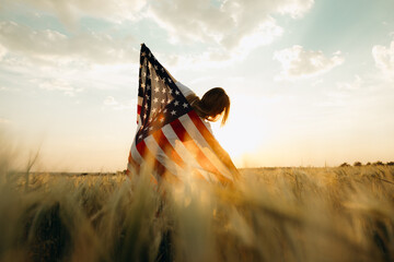 Young woman with American flag in a wheat field at sunset. 4th of July. Patriotic holiday, american...