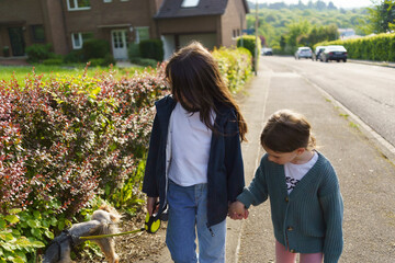 Two little girls holding hands along the street walking their small dog