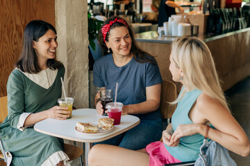 Three women drink cooling lemonades and have lunch while sitting in a cafe on a summer day.