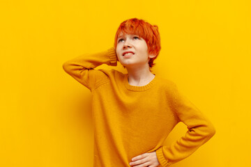 puzzled red-haired teenage boy thinks and chooses on a yellow isolated background, confused child...
