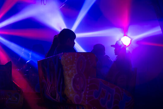 Luces de colores neon y siluetas negras de gente dentro de un juego mecanico en la espera de el inicio.