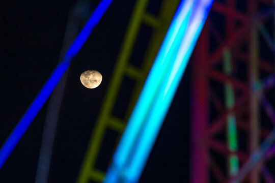 Luna vista a trav&eacute;s de la estructura de un juego mec&aacute;nico iluminado con luces neon