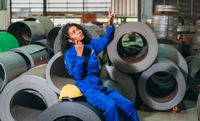 Industrial worker in a blue jumpsuit is talking on a talkie walkie while sitting on a pile of