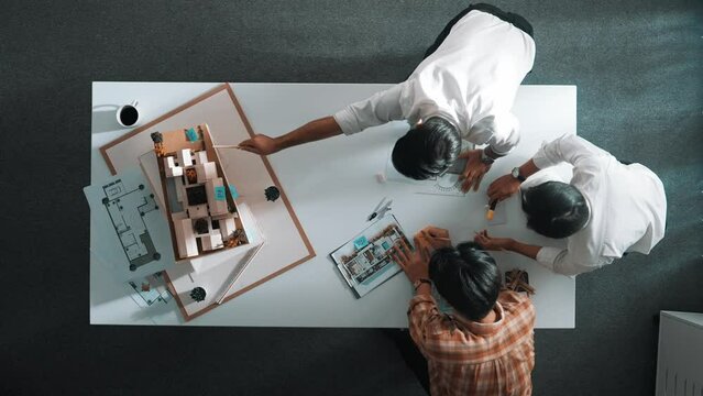 Group of skilled designer looking at model while discussing about building. Top view of architect engineer explain idea while talking and writing blue print scattering at meeting table. Alimentation.