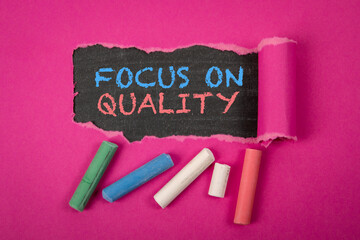 FOCUS ON QUALITY. Text under torn purple paper on a blackboard