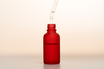 A drop on the end of the pipette of the red dropper bottle wuth face serum