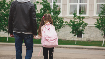 Back to school. Schoolgirl with backpack and father going to school first lesson holding hands back...