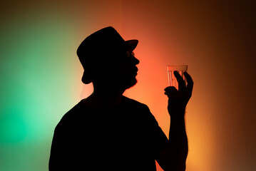 Man in hat in silhouette holding a glass of water