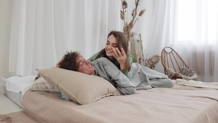 Young couple embraces and relaxes on a cozy bed in a bright room, enjoying peaceful moments together. slow motion, 4k - Powered by Adobe