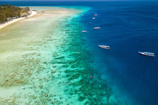 Snorkel and swim tour boats on the edge of a fringing tropical coral reef off a tropical island