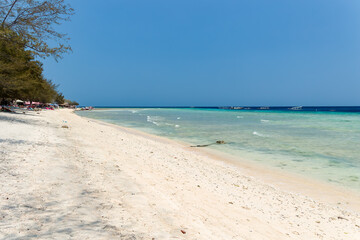 Tropical sandy beach surrounded by fringing coral reef and warm ocean