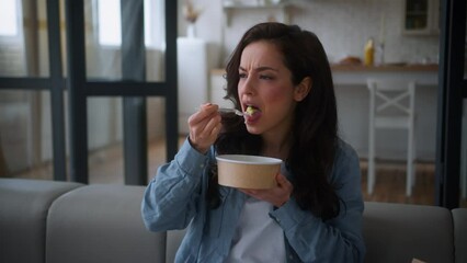 Caucasian woman at home apartment couch sofa female girl eat disgusting bad awful dish tasteless meal food delivery dissatisfied cafe restaurant order client eating spoiled disgust nutrition problem