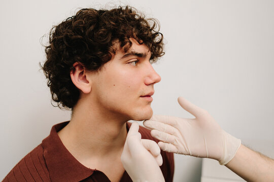Face correction and lifting to reshape chin. Facebuilding. Doctor touching male face in protective gloves before chin shape correction with fillers.
