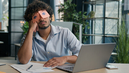 Funny lazy businessman tired male business manager napping at office desk Arabian Indian man sleep closed eyes with sticky notes comical ridiculous stickers on face sleeping guy nap pretend working