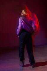 A young woman dances contemporary dances in blue and red light. Long exposure. Vertical photo. 